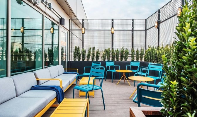 The outdoor seating area at My Lounge, London Gatwick Airport, features tables and chairs surrounded by greenery for relaxation.