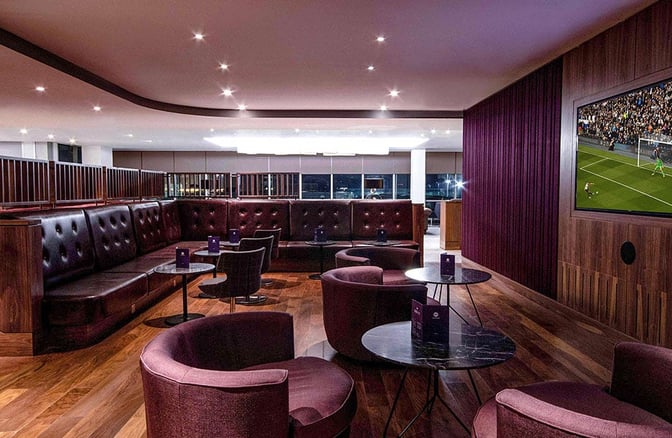 The No1 Lounge at London Gatwick Airport features a seating area with tables and a large screen displaying a sports event.