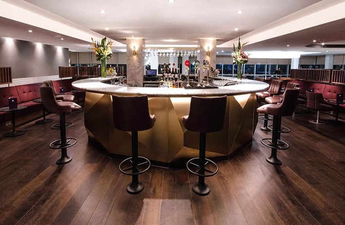 The No1 Lounge at London Gatwick Airport features a central bar with seating, offering a selection of beverages for travelers.