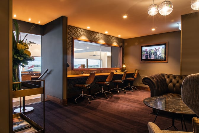 Workspace seating in No1 Lounge at Heathrow Airport features swivel chairs and desks with power outlets, adjacent to a seating area.