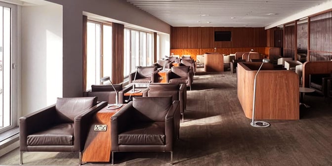 Seating area in Blush Lounge at Heathrow Airport features individual armchairs with side tables and power outlets, offering airport views.