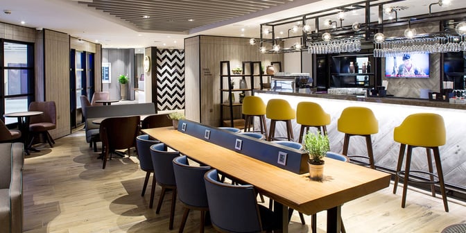 The Plaza Premium Lounge at London Heathrow features a bar with counter seating and a communal table equipped with charging ports.