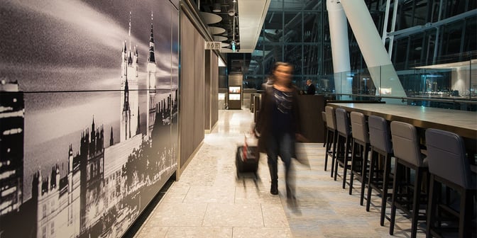 The Plaza Premium Lounge at London Heathrow Airport features high-top seating near a wall mural and adjacent restroom facilities.