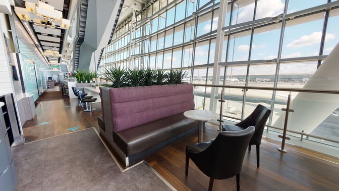 The Club Aspire Lounge at London Heathrow Airport features seating with airport views, including booth and table arrangements for travelers.