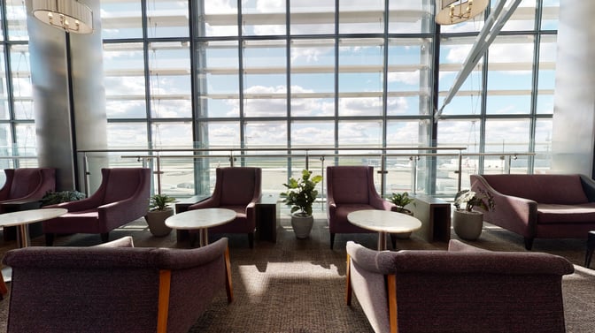 The seating area in Club Aspire Lounge at London Heathrow Airport offers comfortable chairs and tables with expansive airport views.