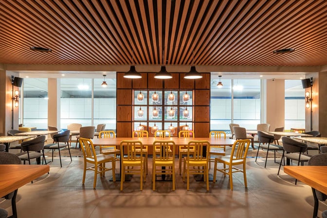 Seating area in My Lounge at London Luton Airport features communal tables and chairs, with decorative lighting and window views.