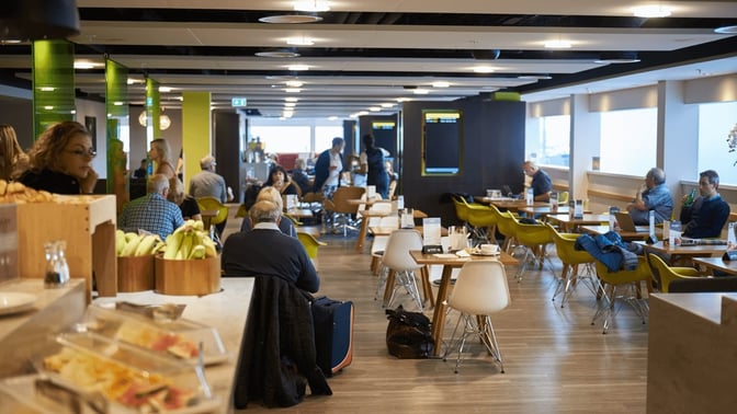 The Escape Lounge at London Stansted Airport features a seating area with tables and chairs, offering a relaxed dining environment.