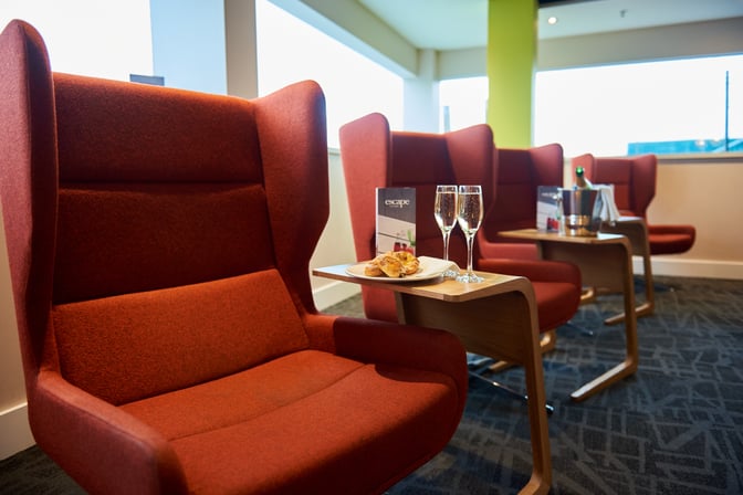 High-backed seating in the Escape Lounge at London Stansted Airport features side tables with snacks and drinks for passenger comfort.