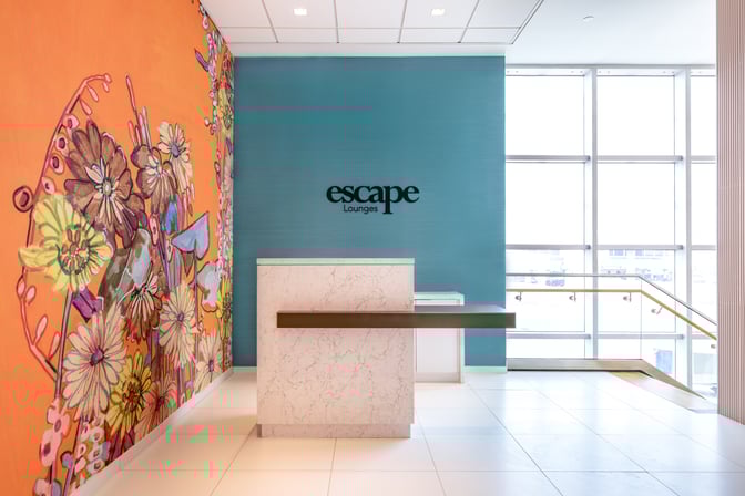 The entrance to the Escape Lounge at Luis Munoz Marín International Airport features a reception desk and vibrant wall art.