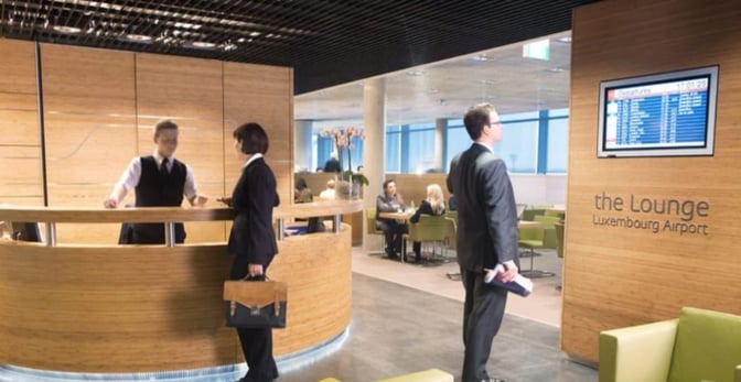 The reception area of The Lounge at Luxembourg Airport features a check-in desk and a flight information display screen.