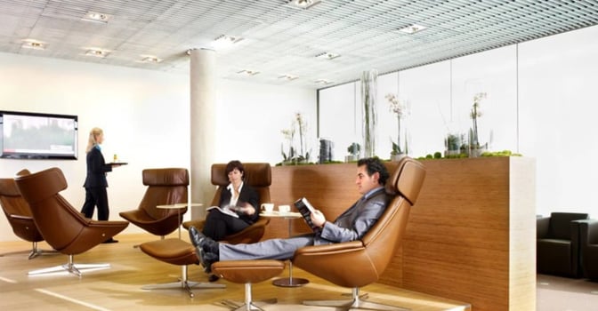 Luxembourg Findel Airport lounge features comfortable seating with individual tables, offering a relaxing space for passengers to read or enjoy refreshments.
