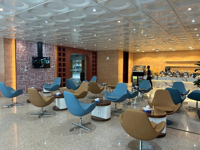The Pearl Lounge at Luxor International Airport features a seating area with swivel chairs and a buffet offering various refreshments.
