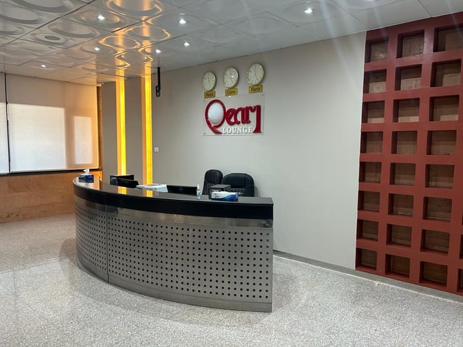 The reception area of Pearl Lounge at Luxor International Airport features a curved desk with seating and wall clocks displaying global times.