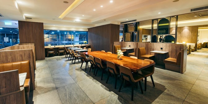 The Plaza Premium Lounge at Macau International Airport features communal and booth seating areas with tables for dining and work.