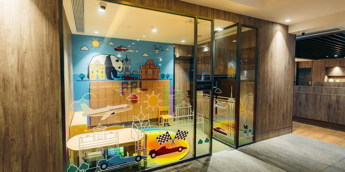 The children's play area at Plaza Premium Lounge, Macau International Airport, features colorful wall art and small tables with chairs.