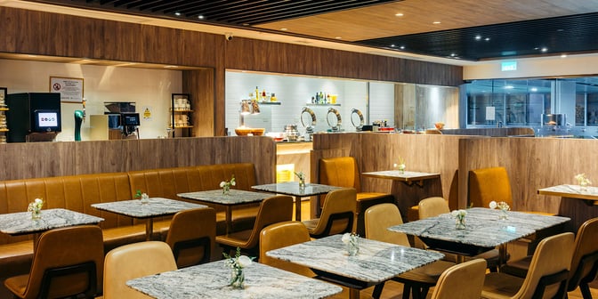 The dining area at Plaza Premium Lounge, Macau International Airport, features dining table seating and a self-serve food and beverage station.