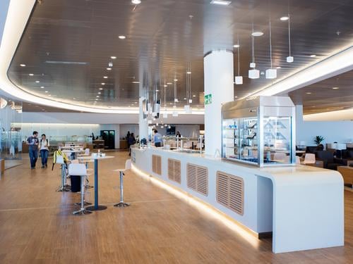 The Sala Cibeles lounge at Madrid Barajas Airport features a spacious self-service food and beverage area with seating options.