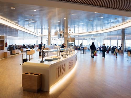 The Sala Cibeles lounge at Madrid Barajas Airport features a central self-serve food station with seating areas for travelers.