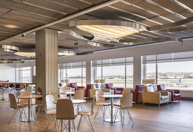 The seating area in Sala Puerta De Alcalá at Madrid Barajas Airport offers tables and chairs with views of the runway.