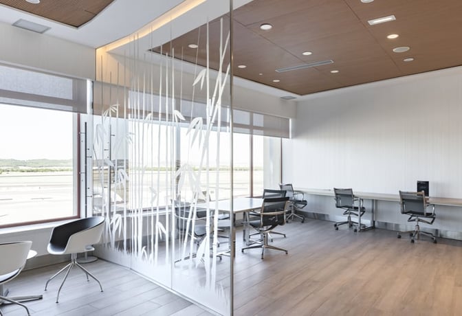 The Sala Puerta De Alcalá at Madrid Barajas Airport features a workspace with desks, chairs, and views of the runway.