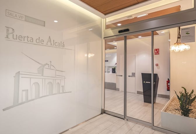 The entrance to Sala Puerta De Alcalá at Madrid Barajas Airport features sliding glass doors and a reception area visible inside.