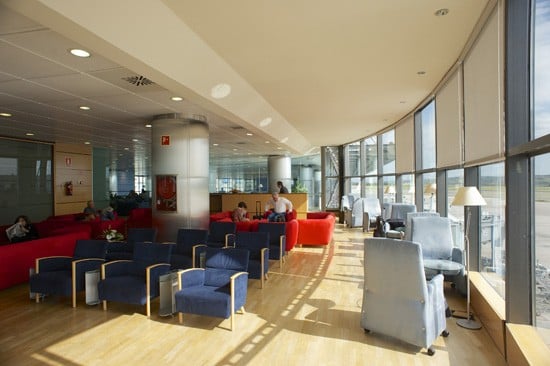 The seating area in Sala Puerta Del Sol at Madrid Barajas Airport offers armchairs with views of the tarmac through large windows.