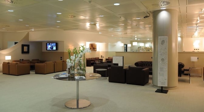 The Monteverdi Classic Lounge at Malpensa Airport features comfortable seating areas with a television and a central table with magazines.