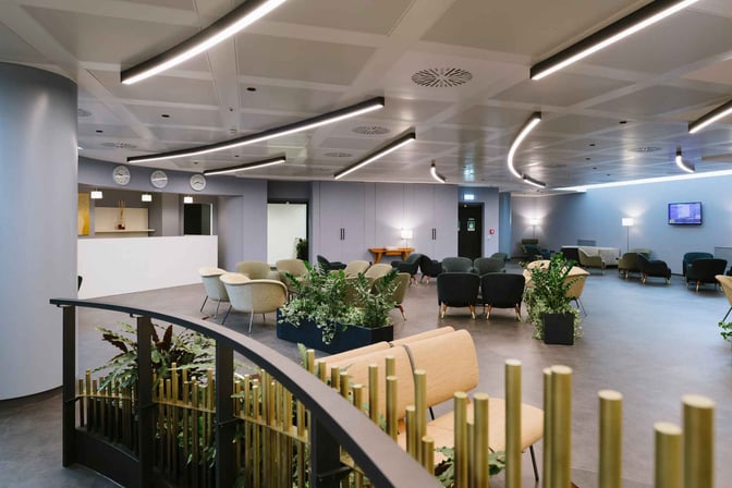 The Monteverdi Classic Lounge at Malpensa Airport features a spacious seating area with various chairs and tables, surrounded by greenery.