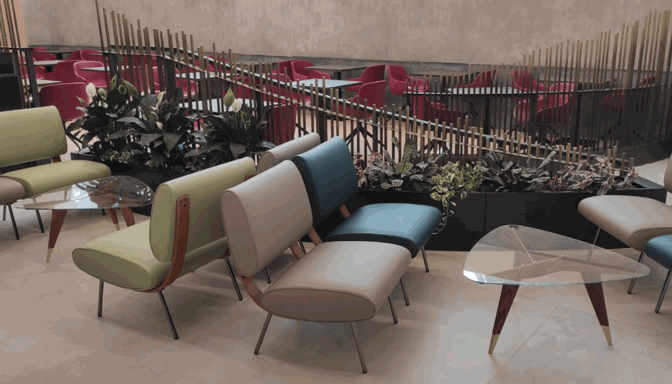 The seating area in Pergolesi Classic Lounge at Malpensa Airport features cushioned chairs, glass tables, and decorative plants for passenger comfort.