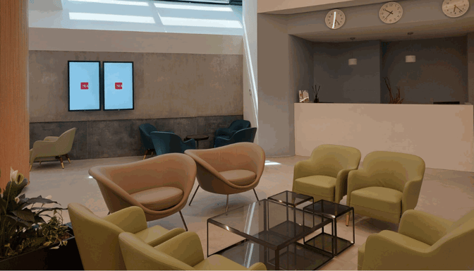 The Pergolesi Classic Lounge at Malpensa Airport features a seating area with armchairs and tables, adjacent to a reception desk.