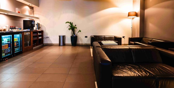 The VIP Lounge at Malta International Airport features a seating area with leather sofas and a self-serve beverage station.