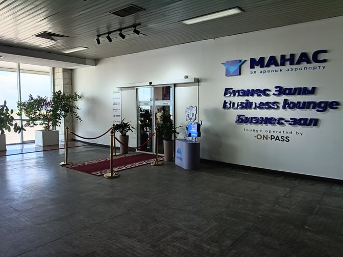 The entrance to the Business Lounge at Manas International Airport features a red carpet and signage indicating lounge access.