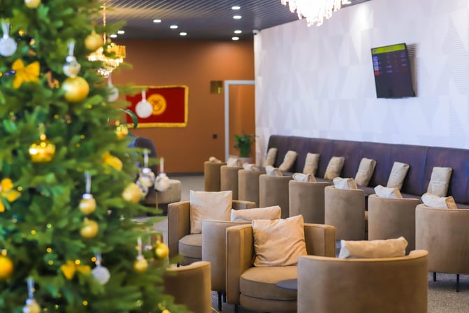 Seating area in the Manas International Airport Business Lounge features cushioned chairs and a wall-mounted flight information display.
