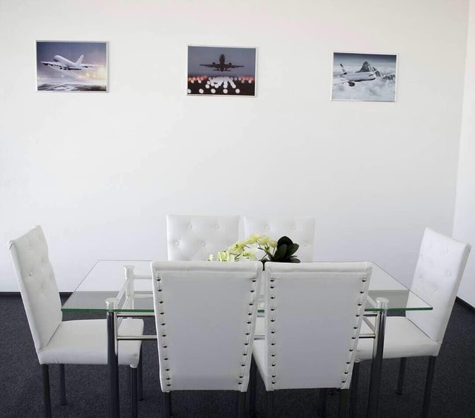 A seating area in Manas International Airport's business lounge features a glass table with cushioned chairs and aviation-themed wall art.
