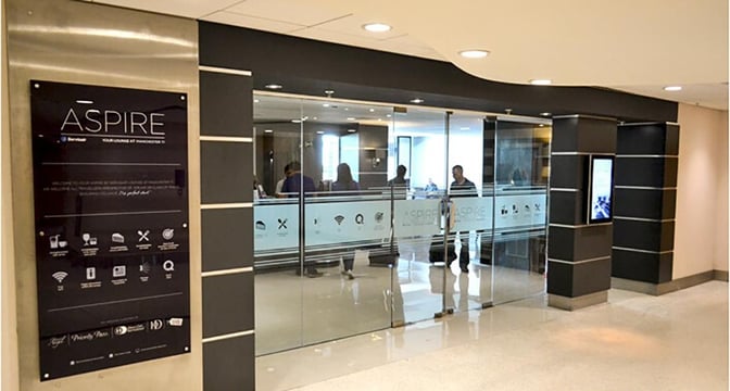 The Aspire Lounge entrance at Manchester Airport features glass doors and signage displaying available amenities and services.