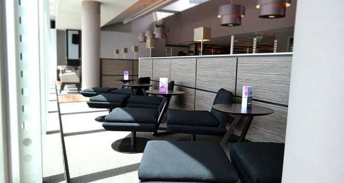 The Aspire Lounge at Manchester Airport features comfortable seating with small tables, providing a relaxing space for travelers.