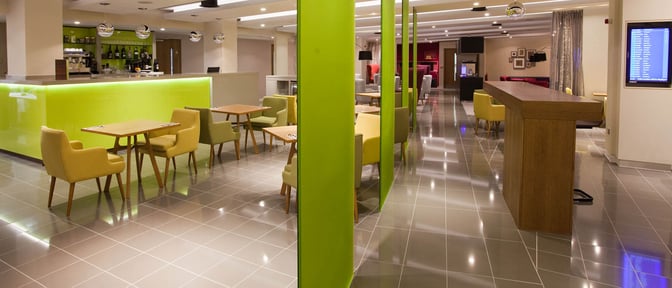 The Escape Lounge at Manchester Airport features a bar with complimentary beverages and a seating area with tables and chairs.