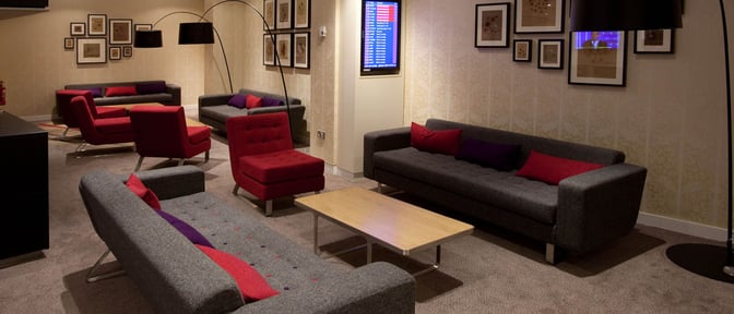 The seating area in Manchester Airport's Escape Lounge features comfortable sofas and armchairs with a flight information screen.
