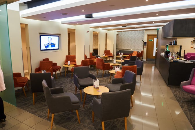 The seating area in Manchester Airport's Escape Lounge features comfortable chairs and tables, with a television for entertainment.