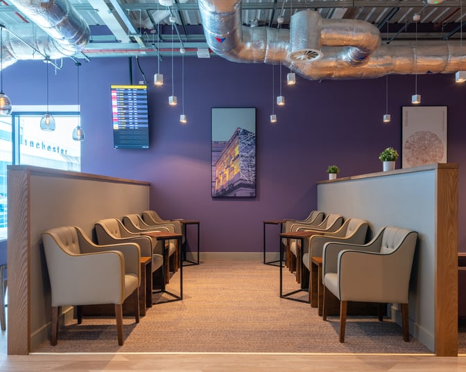 The Aspire Lounge at Manchester Airport features a seating area with individual chairs and tables, alongside a flight information screen.