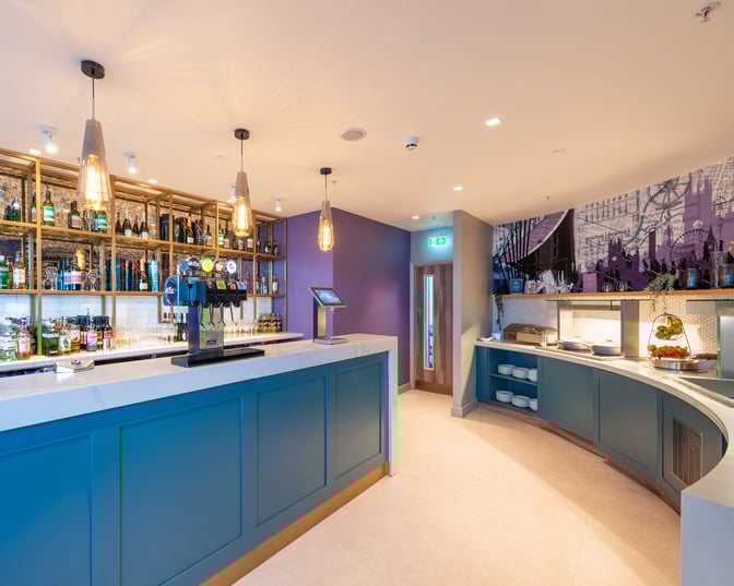 The Aspire Lounge at Manchester Airport features a bar with a variety of beverages and a self-serve food area.