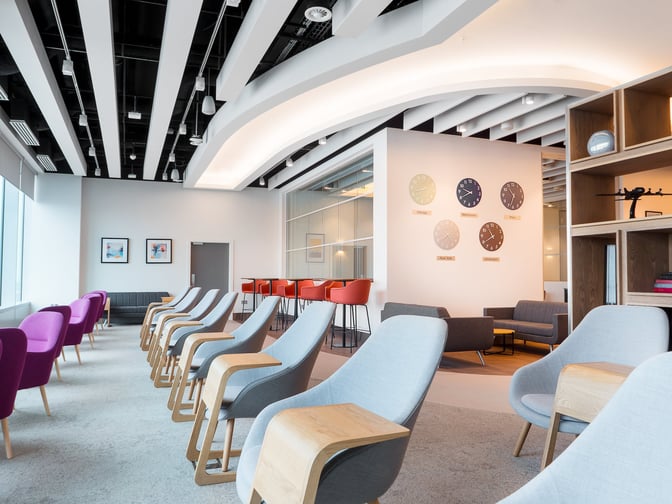 The seating area in Manchester Airport's Escape Lounge features comfortable chairs and sofas with wall clocks displaying various time zones.
