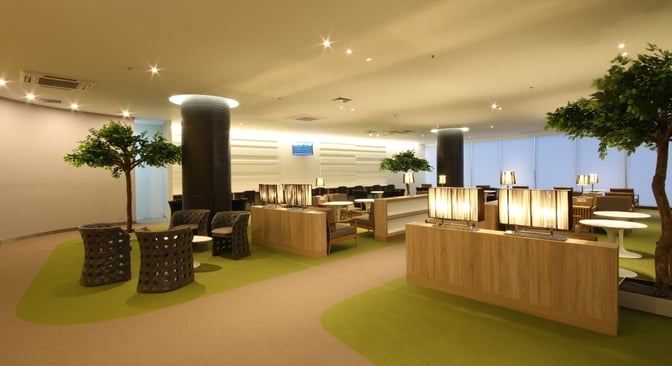 The CIP Lounge at Mandalay International Airport features seating areas with tables and lamps, surrounded by decorative plants for relaxation.