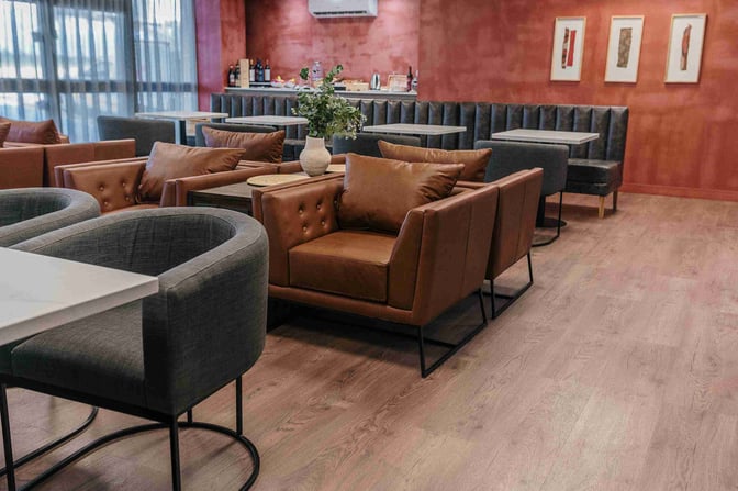 The seating area at Salta by AMAE Lounge features comfortable chairs and tables, with a view of the airport through large windows.