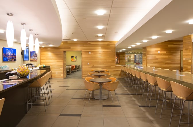 The Club LAS at McCarran International Airport features a seating area with tables, bar stools, and snacks available on the counter.