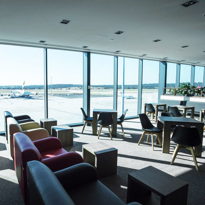 The Marhaba Lounge at Melbourne Airport features seating with tables and chairs, offering views of the airport runway through large windows.