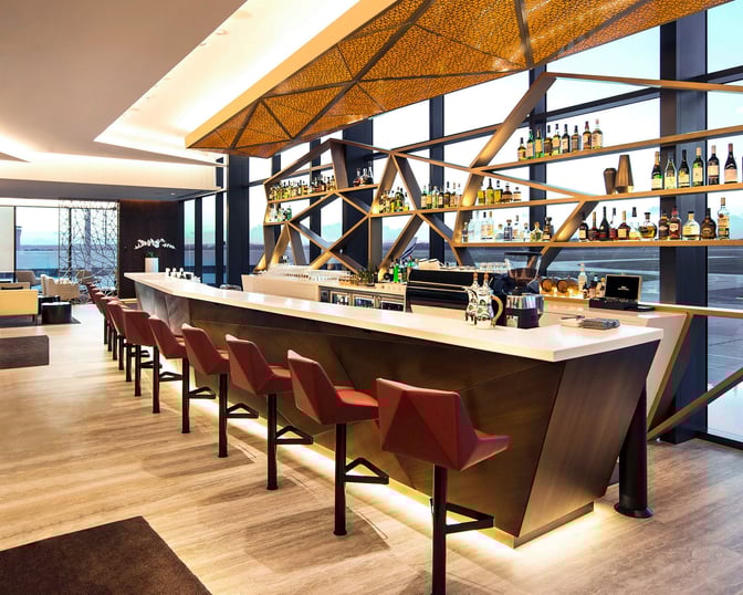 The bar at The House by Aspire in Melbourne Airport features a counter with seating and a selection of displayed spirits.