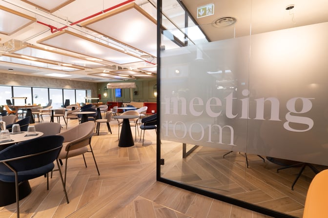 The HelloSky lounge at Milan Bergamo Airport features a seating area with tables and chairs adjacent to a meeting room.