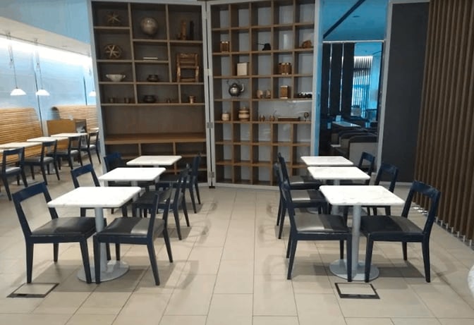 The seating area in LATAM Lounge at Ministro Pistarini International Airport features tables and chairs adjacent to decorative shelving.
