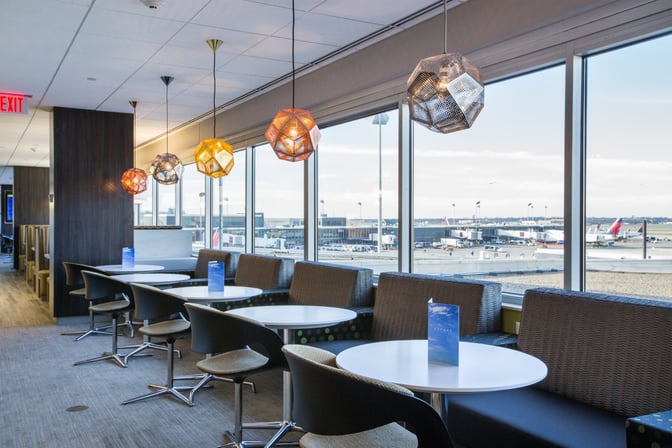 Seating area in the Escape Lounge at Minneapolis-Saint Paul International Airport offers tables with airport views and overhead lighting.
